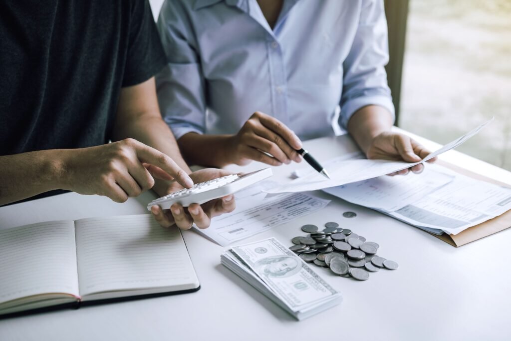 Two people analyzing bills and finances, with calculator, money, and coins on the table.