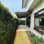 Exterior view of a house with a covered patio, lush greenery, and a walkway.