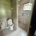 A modern bathroom with gray tile, a toilet, and a shower stall with a window.