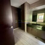 A modern bathroom with brown cabinets, a black sink, and light gray tile flooring.