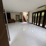 A wide view of a modern, empty living room with white tile floors and a dining area in the background.