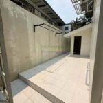 A narrow outdoor space with tiled flooring and a tall, textured wall.