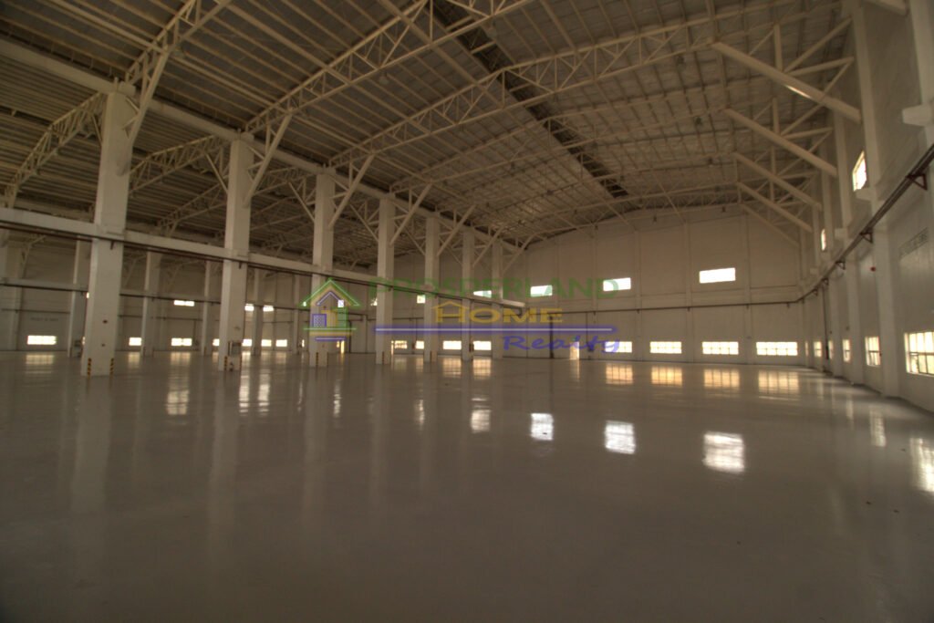 Interior view of a large, empty warehouse with high ceilings and structural beams.