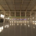 Interior view of a large, empty warehouse with a high ceiling and polished floor.