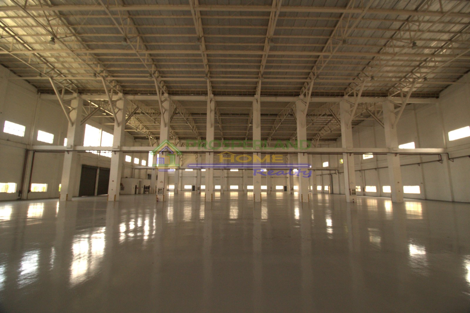 Interior view of a large, empty warehouse with a high ceiling and polished floor.