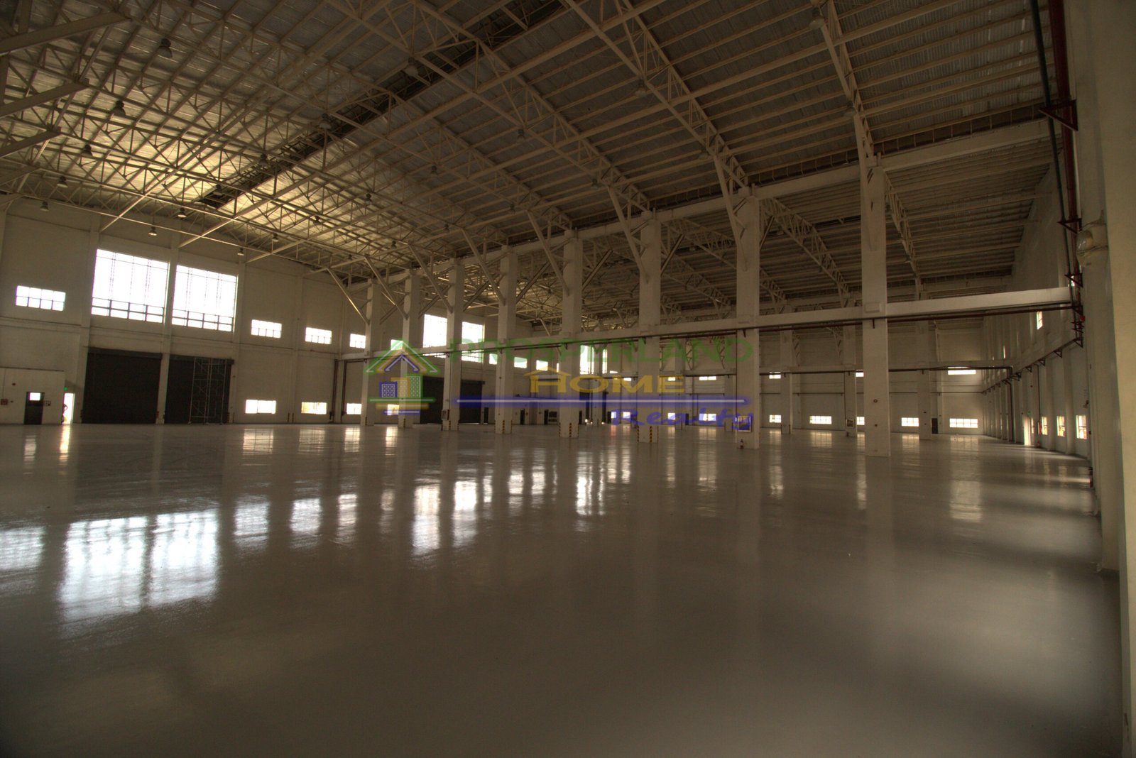 Interior of a large, empty warehouse with a metal roof and concrete floor.