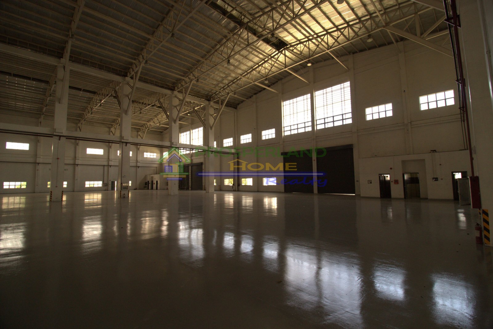 Interior view of a large, empty warehouse with high ceilings and a polished floor.
