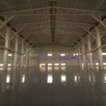 Interior view of a large, empty warehouse with a high ceiling and polished floor.
