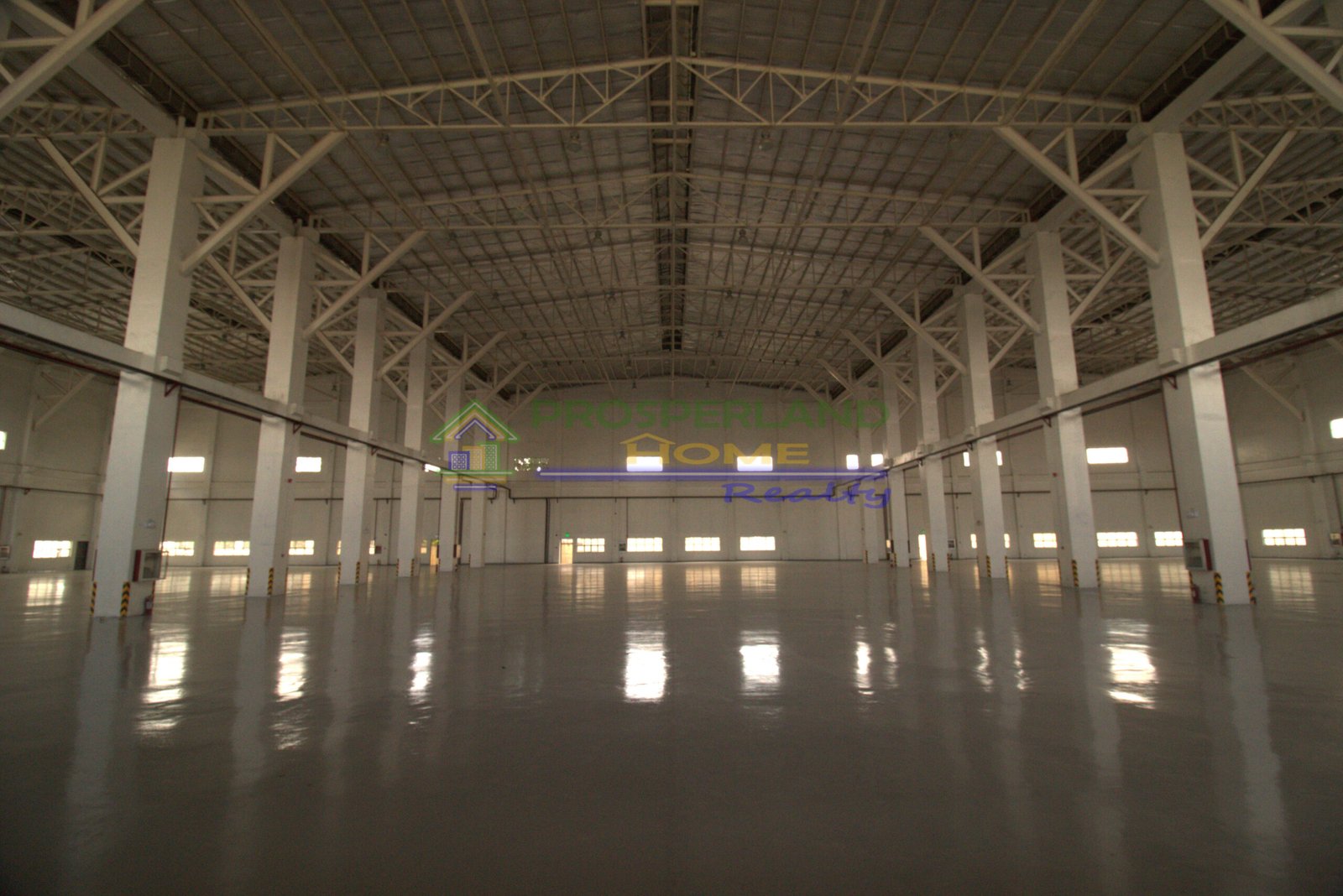 Interior view of a large, empty warehouse with a high ceiling and polished floor.