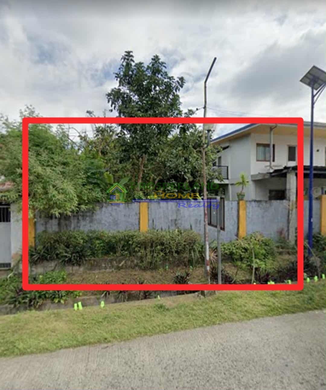 Image of a property lot outlined in red, with a concrete fence, trees, and a house visible in the background.