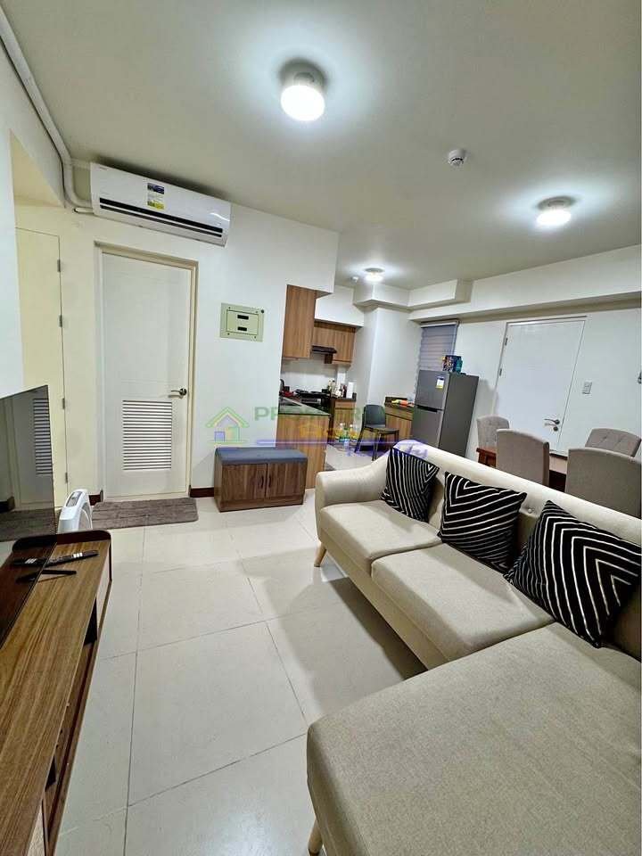 A bright, modern apartment interior with a sectional sofa, dining area, and kitchen.