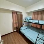 A bedroom with wooden floors, a bunk bed with blue bedding, a wardrobe, and a curtain.