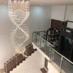 Interior view of a home with a large spiral crystal chandelier over a staircase and an exercise area visible on a landing.