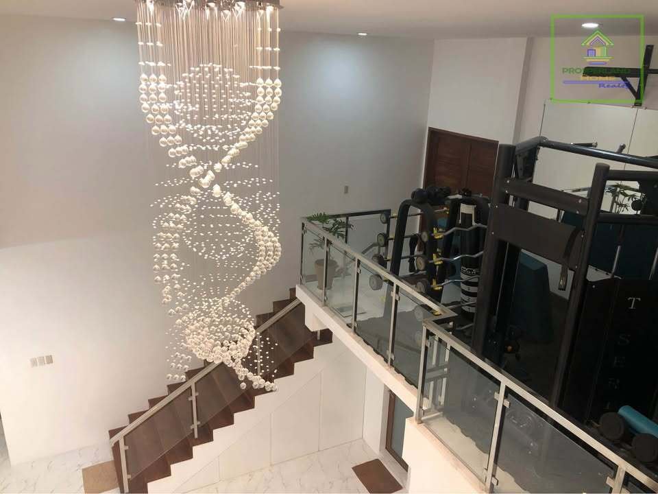 Interior view of a home with a large spiral crystal chandelier over a staircase and an exercise area visible on a landing.