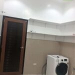Laundry room with white washing machine, shelving, tile walls, and dark wood door.