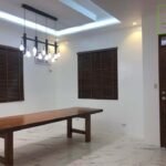 A well-lit modern room with a long wooden table, brown blinds, and a unique chandelier.
