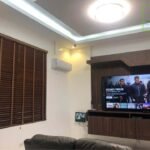 A living room with dark wood blinds, a TV playing "Ocean's Twelve," and modern recessed lighting.