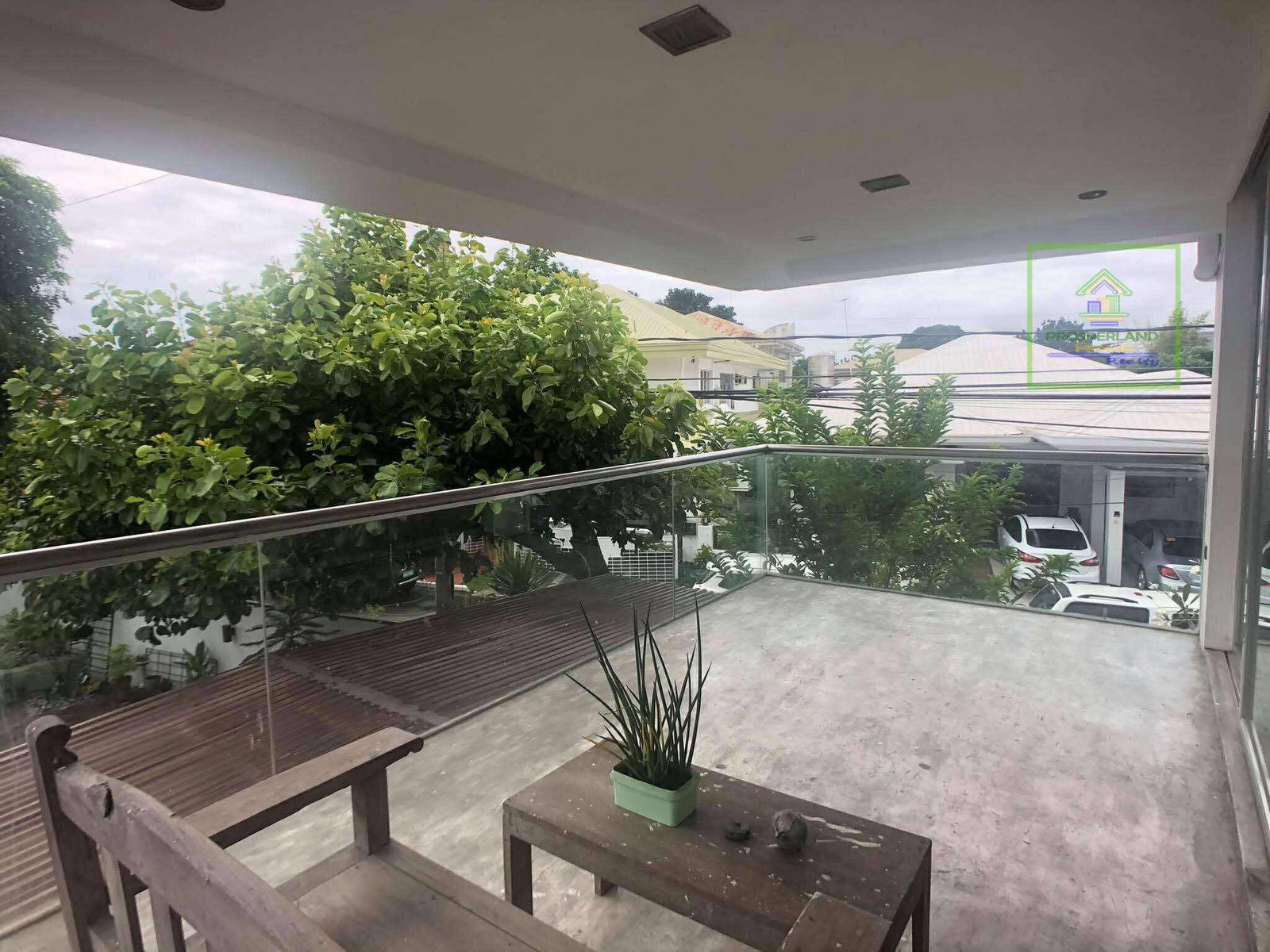 Balcony with glass railings overlooking a neighborhood and lush greenery.