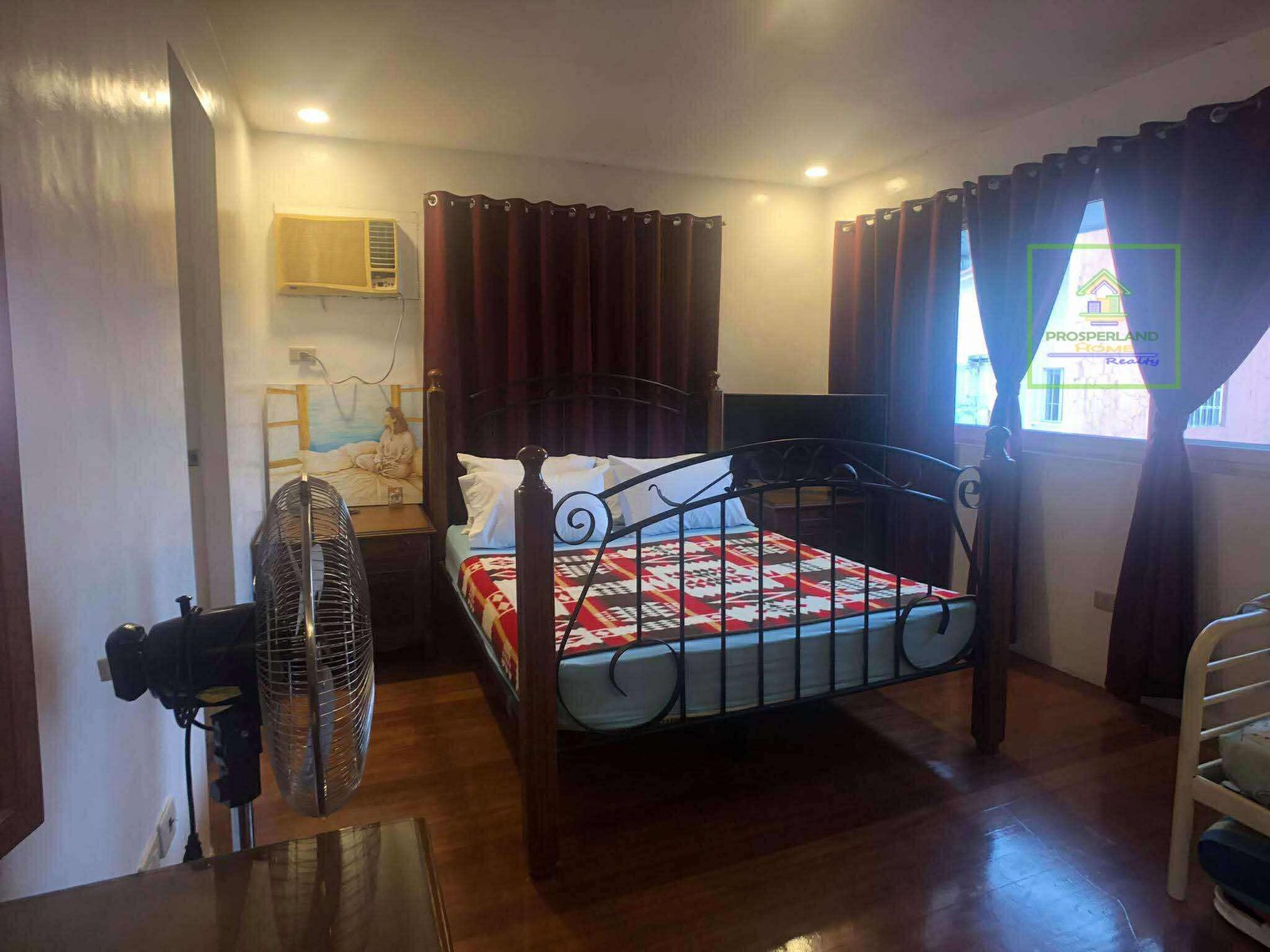 Bedroom with a metal bed frame, red and white patterned blanket, and dark curtains.