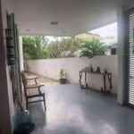 Covered patio with outdoor furniture, plants, and view of greenery.