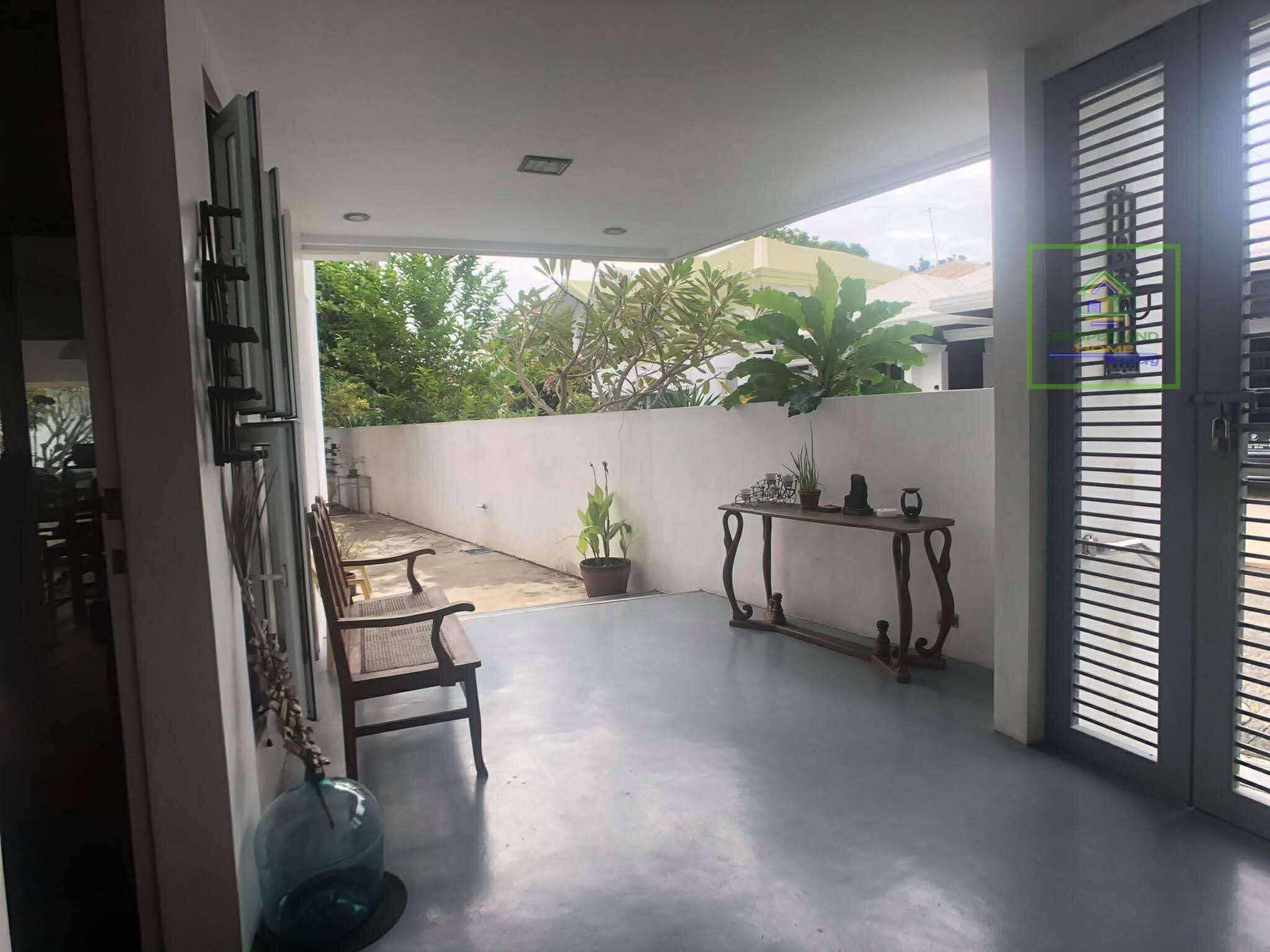 Covered patio with outdoor furniture, plants, and view of greenery.