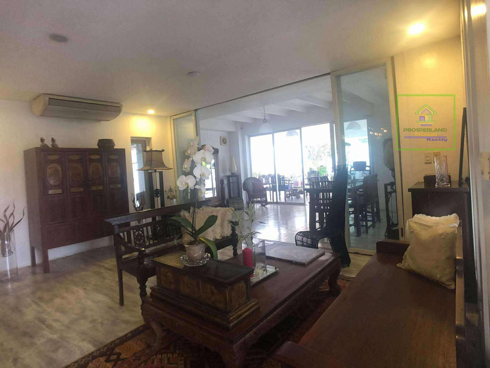 A living room with dark wood furniture, large glass doors, and an outdoor view.