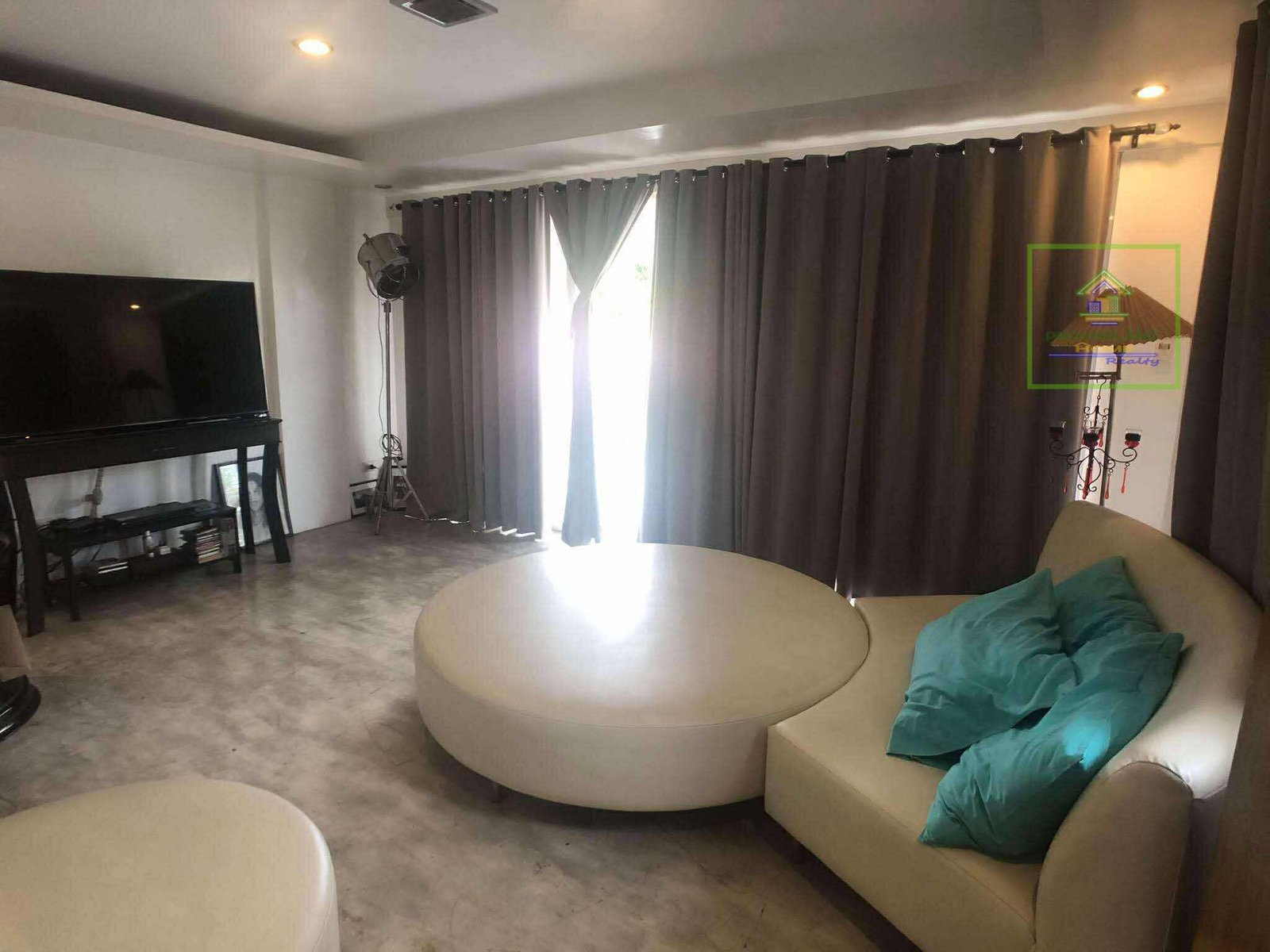 Modern living room featuring a round sofa, TV, and large windows with curtains.