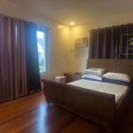 A bedroom with a woven bed frame, hardwood floors, and brown curtains.