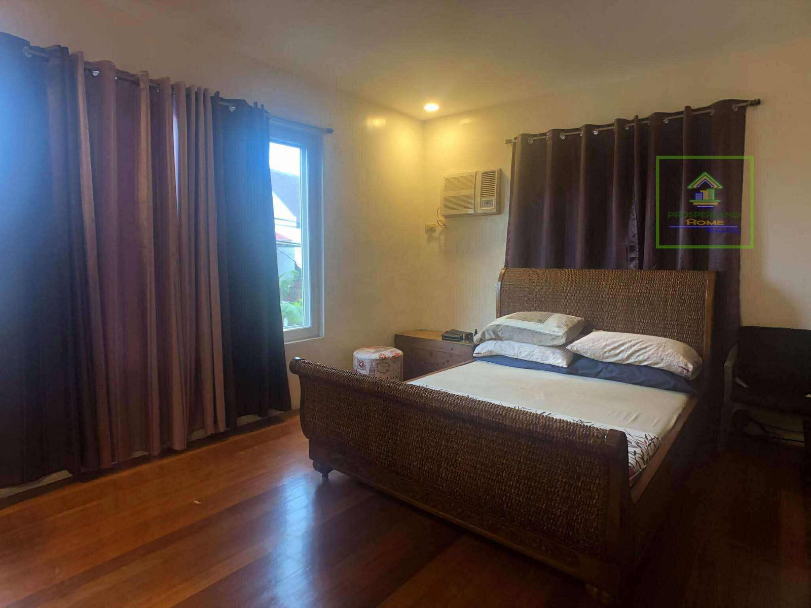 A bedroom with a woven bed frame, hardwood floors, and brown curtains.