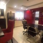 Interior view of a dining area with kitchen, featuring dark wood table and red upholstered chairs.