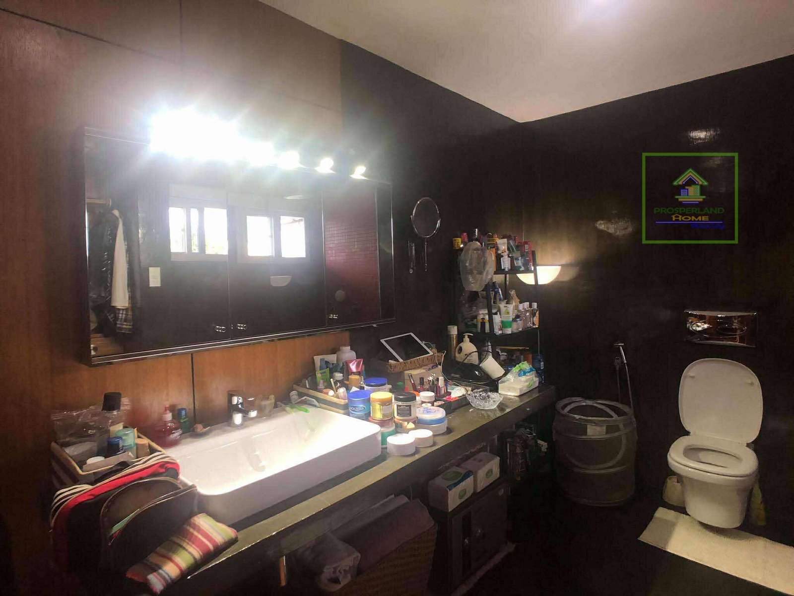 A cluttered bathroom with a large mirror, sink, and toilet.