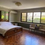 Bedroom with a wooden bed, hardwood floors, barred windows, and chairs by a window.