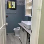 A modern bathroom with gray tiles, a white sink, a cabinet, and a toilet.