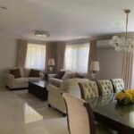 A well-lit living and dining room with beige couches and chairs.