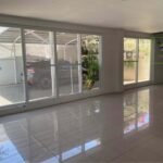 A bright, empty room with large windows, shiny tile floor, and a view of a parked car and greenery.