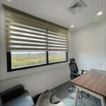 Office space with desk, chair, and sofa near a window with horizontal blinds.