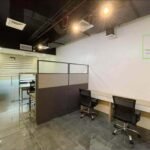 An office space with desks, chairs, dividers, glass-enclosed area, and the Prosperland Realty logo.
