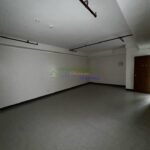 An empty room with gray floors, white walls, exposed pipes, and a door.