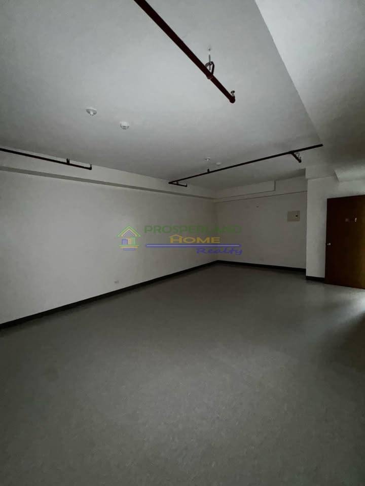 An empty room with gray floors, white walls, exposed pipes, and a door.
