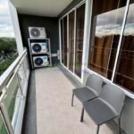 A balcony with two gray chairs, sliding glass doors, and air conditioning units.