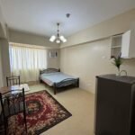 Studio apartment with bed, table, rug, refrigerator, and minimalist decor.