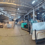A wide shot shows a warehouse interior filled with stacked, crated glass and a forklift.