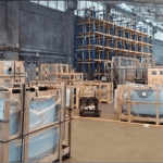 Warehouse interior filled with crates containing glass panels, and a Prosperland Home Realty logo overlay.