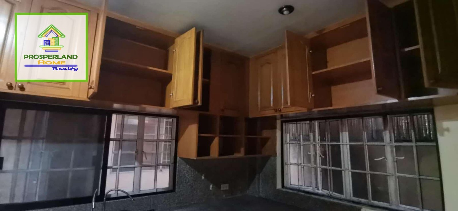 A kitchen with wooden cabinets and a window, with a real estate logo in the corner.