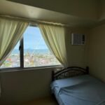 Bedroom with a view of a cityscape, ocean, and construction crane through a window.