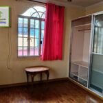 Bedroom with wood floors, a window with red curtains, a small table, and a sliding-door closet.