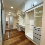 Walk-in closet with built-in white cabinetry and hardwood floors.