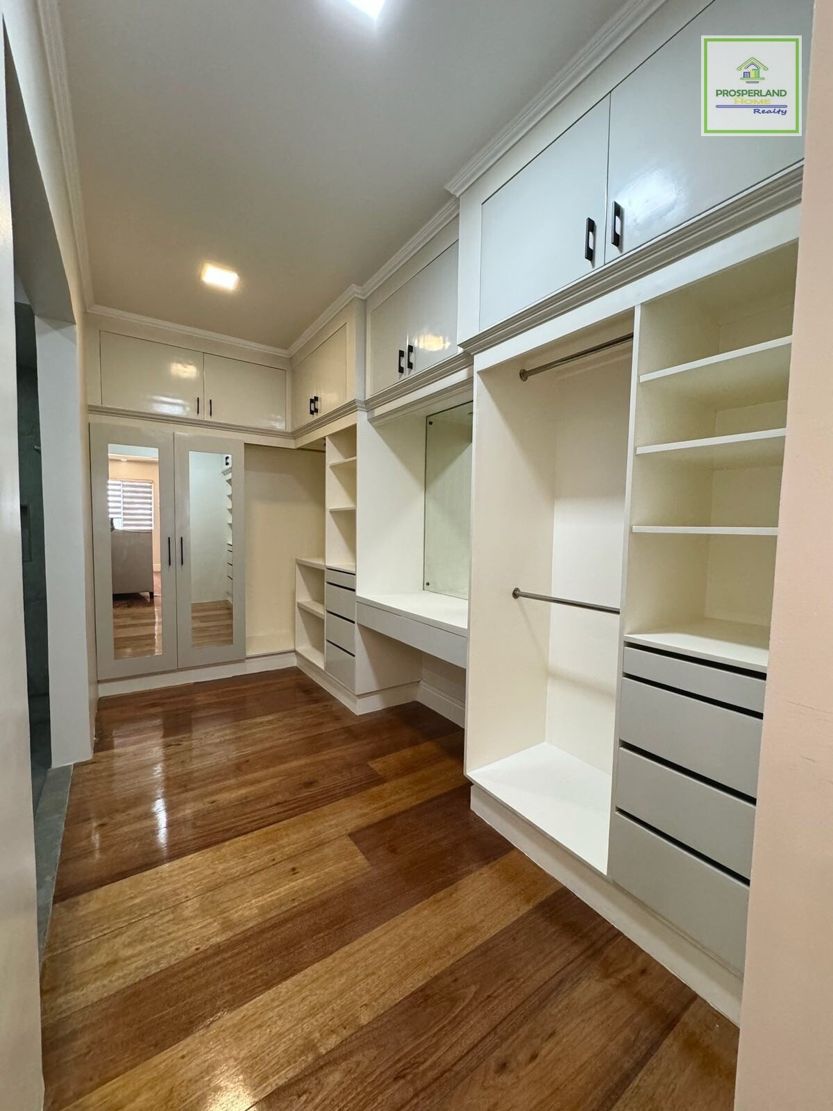 Walk-in closet with built-in white cabinetry and hardwood floors.