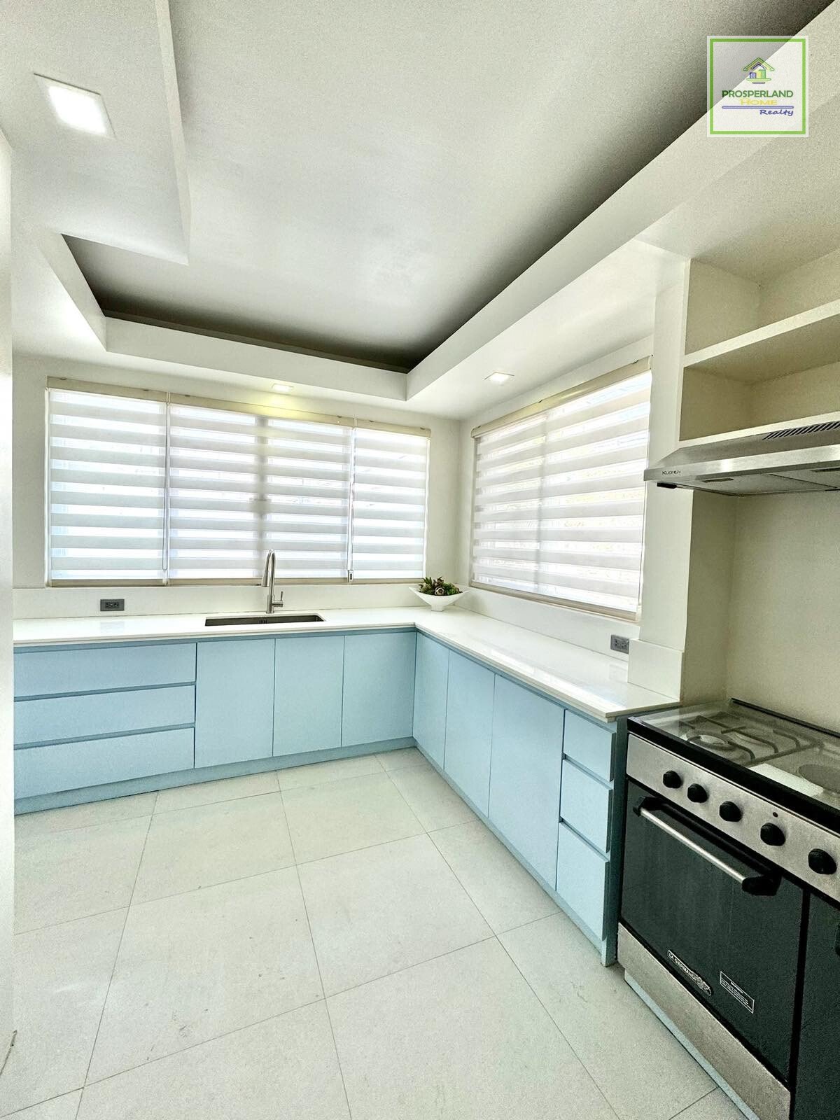 A bright, modern kitchen with light blue cabinets, white countertops, and a gas stove.
