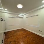 An empty room with parquet floors and two windows with white blinds.